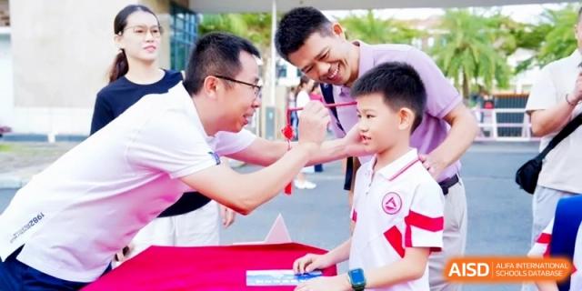 A smiling teacher or parent interacts with a young student in a white uniform during an outdoor school community event at RDFZ Sanya School