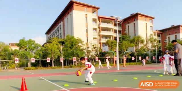 A young student practices dribbling a basketball between cones on an outdoor sports court during a training session at RDFZ Sanya School