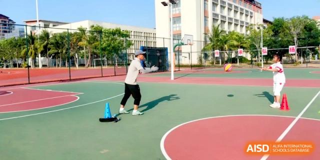 A student in athletic gear prepares to throw a ball on an outdoor court with school buildings in the background at RDFZ Sanya School