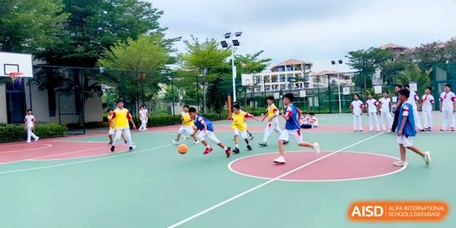 A group of students plays a fast-paced basketball game on a green and red outdoor court under a clear sky at RDFZ Sanya School