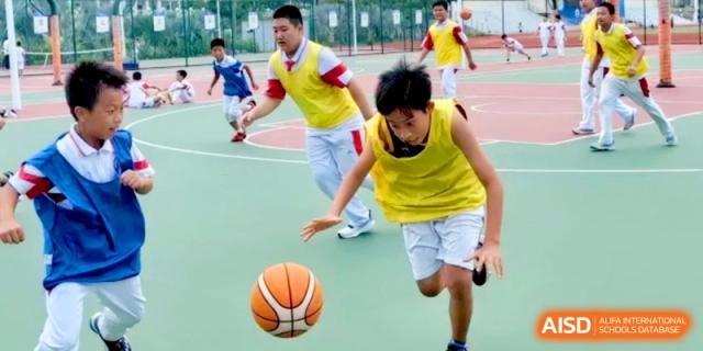 Two students in yellow jerseys compete for the ball during an energetic basketball game on an outdoor court at RDFZ Sanya School