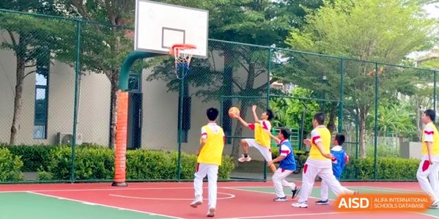A student in a yellow vest leaps to take a shot at the basket during an outdoor physical education class at RDFZ Sanya School