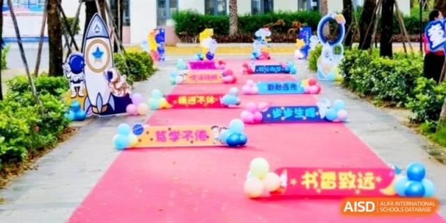 A vibrant pink carpet lined with colorful balloons and signs creates a festive walkway for a school event at RDFZ Sanya School