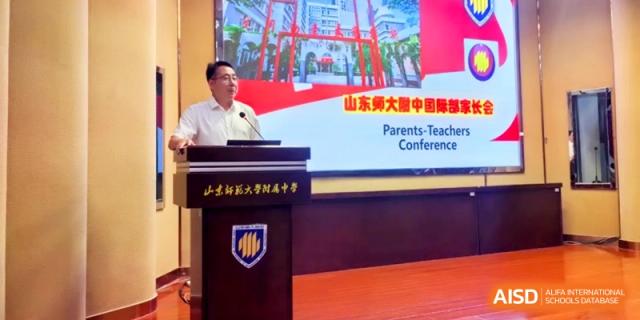 A speaker stands at a podium during a Parents-Teachers Conference in a large hall at the Attached Senior School Of Shandong Normal University.