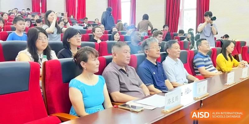 A row of adults and staff members listen intently during a formal school meeting at the Attached Senior School Of Shandong Normal University.