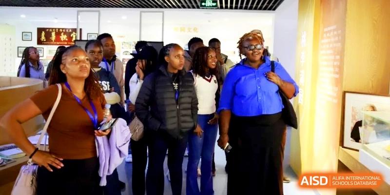 A group of diverse international visitors or students stands together in a hallway at the Attached Senior School Of Shandong Normal University.