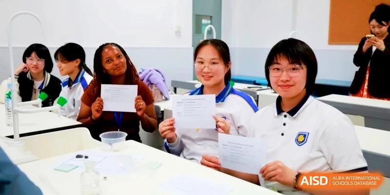 Three smiling students show off their completed worksheets during a classroom lesson at the Attached Senior School Of Shandong Normal University.