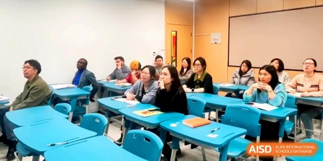 Students and staff sit at blue desks during an informational meeting or seminar at the Attached Senior School Of Shandong Normal University.