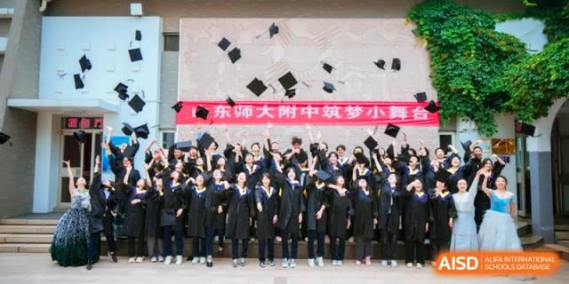 A large group of graduates in caps and gowns toss their hats in the air to celebrate at the Attached Senior School Of Shandong Normal University.