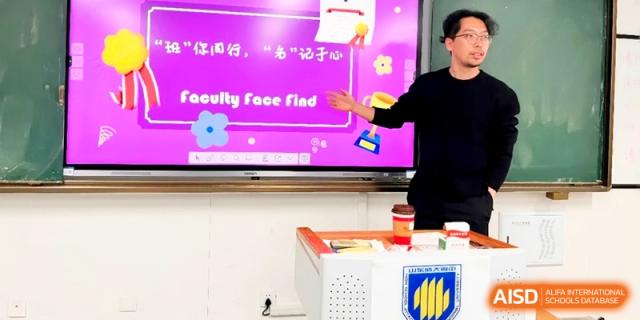 A teacher gestures toward a vibrant "Faculty Face Find" interactive screen in a classroom at the Attached Senior School Of Shandong Normal University.