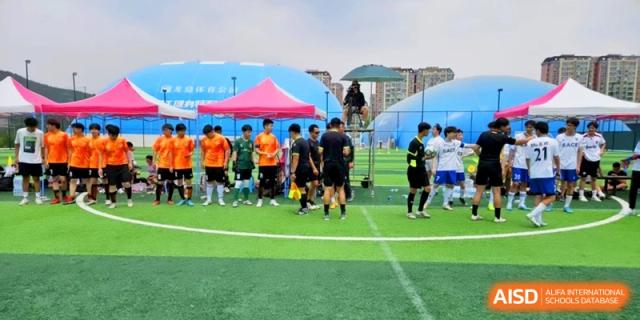Players and coaches gather on the green turf field under a bright sky for a football match at the Attached Senior School Of Shandong Normal University.