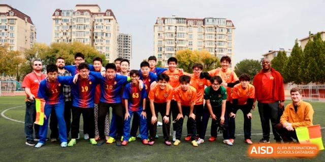 A team of young soccer players in orange and blue jerseys poses for a group photo at the Attached Senior School Of Shandong Normal University.