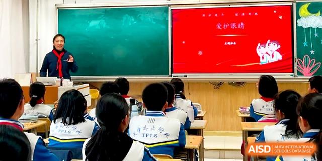 Students in school uniforms sit at their desks facing a bright red presentation screen in class at Tianjin Foreign Languages School.