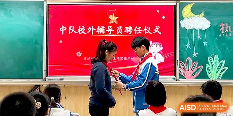 A student participates in a formal red scarf ceremony in front of a celebratory red backdrop at Tianjin Foreign Languages School.