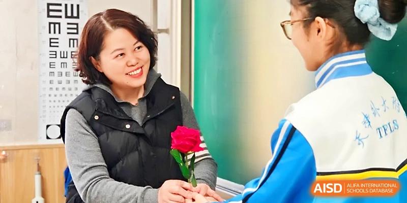 A female staff member smiles warmly while receiving a red rose from a student at Tianjin Foreign Languages School.