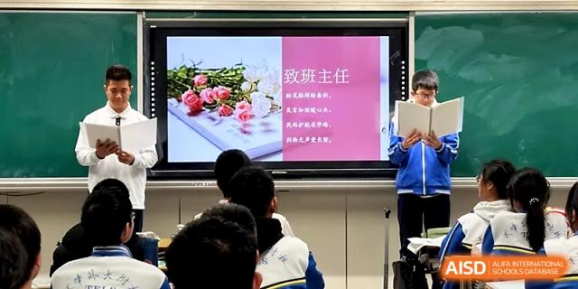 Students watch a presentation on a large monitor featuring floral imagery and Chinese text at Tianjin Foreign Languages School.