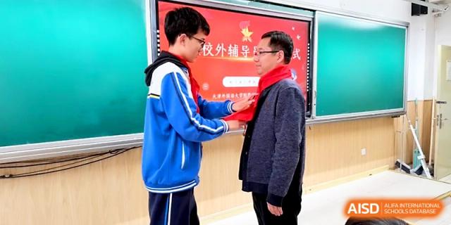 A student carefully ties a red scarf on a male teacher during a celebratory school event at Tianjin Foreign Languages School.