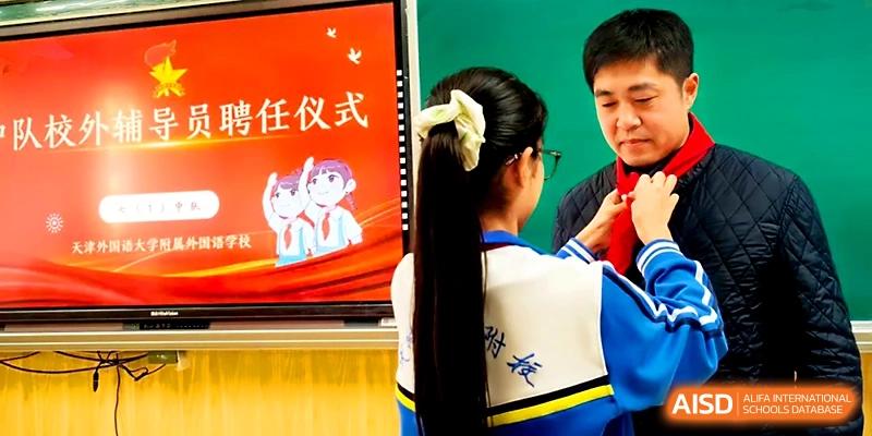 A close-up of a student with a ponytail participating in a traditional red scarf tying ceremony at Tianjin Foreign Languages School.