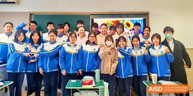 A group of students in blue tracksuits poses for a cheerful group photo in their classroom at Tianjin Foreign Languages School.