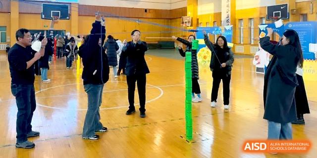 Students engage in a collaborative teamwork exercise using green poles in the sports hall at Tianjin Foreign Languages School.