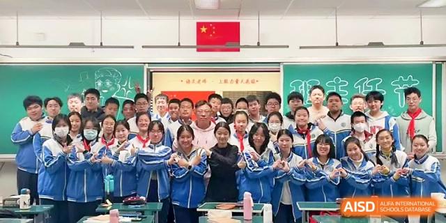 A large group of students and faculty members pose together under the national flag in a classroom at Tianjin Foreign Languages School.