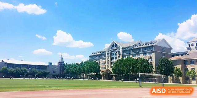 A wide view of the expansive athletic field and multi-story school buildings on a sunny day at Tianjin Foreign Languages School.