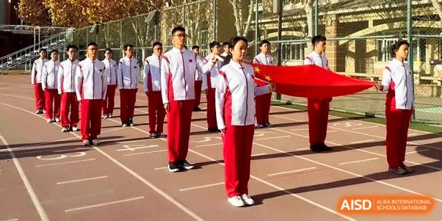 Students in red and white athletic uniforms stand in formation during an outdoor ceremony on the school track at Tianjin Foreign Languages School.