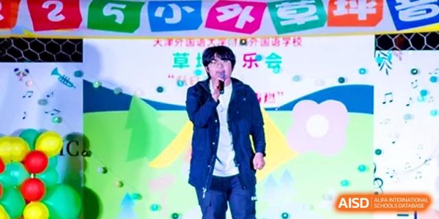 A male student in a dark blue jacket sings a solo under the bright stage lights of a school concert at Tianjin Foreign Languages School.