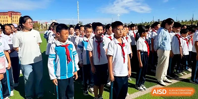 Students in school uniforms with red scarves stand in formation during an outdoor ceremony at Urumqi Bayi High School.