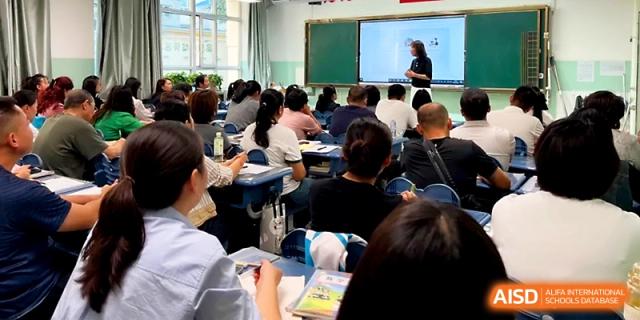 Parents sit in a classroom while a teacher leads a meeting using a digital whiteboard at Urumqi Bayi High School.
