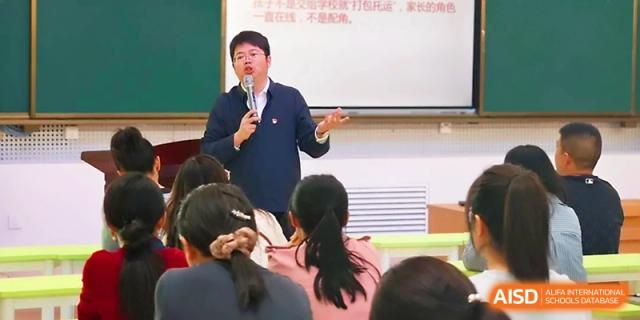 A male staff member speaks into a microphone during a school presentation or meeting at Urumqi Bayi High School.