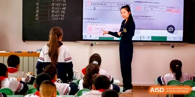 A teacher points to a digital screen while conducting an interactive lesson for primary students in a classroom at Urumqi Bayi High School.
