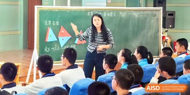 A female teacher gestures toward a chalkboard while explaining a lesson to her students at Urumqi Bayi High School.