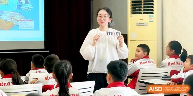 A smiling teacher holds up a small card while engaging with a group of young students during class at Urumqi Bayi High School.