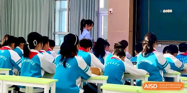 Primary students in blue and white jackets participate in a classroom activity with their teacher at Urumqi Bayi High School.