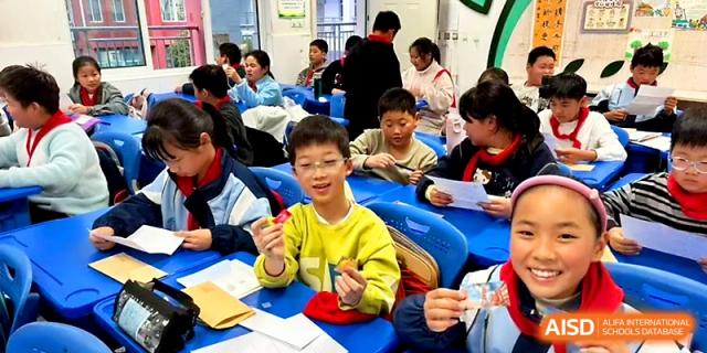 A young boy in a yellow shirt smiles while showing off his craft project during a classroom session at Urumqi Bayi High School.