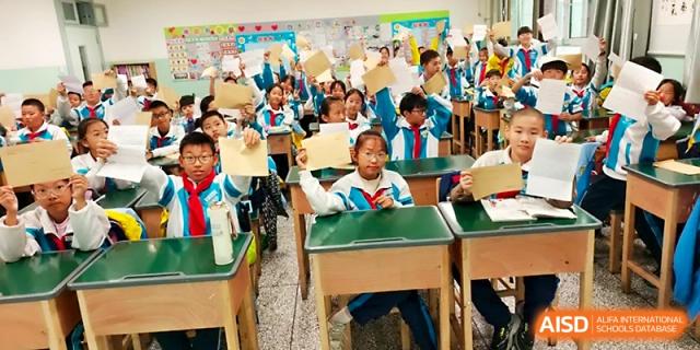A student at the front of the classroom raises her hand to answer a question during a lively lesson at Urumqi Bayi High School.
