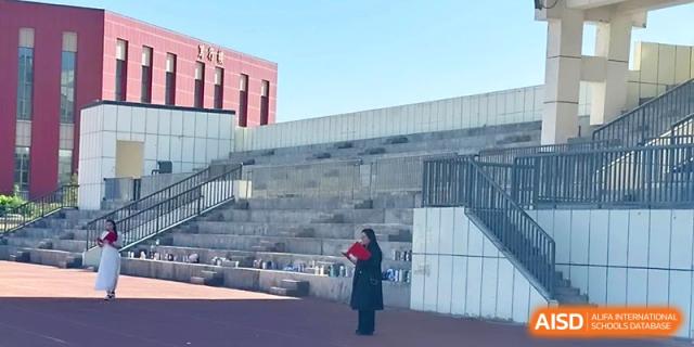 A person stands near the concrete bleachers of the outdoor athletic field on a sunny day at Urumqi Bayi High School.