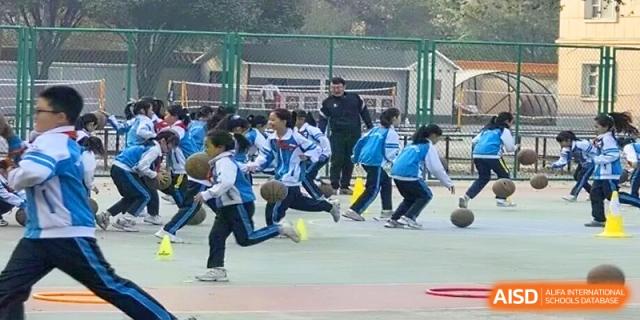 Students in blue uniforms practice basketball drills on an outdoor court during physical education at Urumqi Bayi High School.