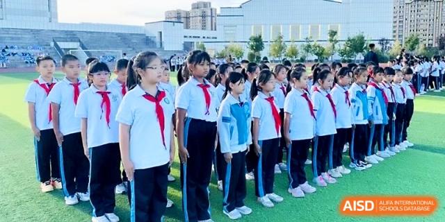 A row of students in white shirts and red scarves stands at attention during an outdoor event at Urumqi Bayi High School.