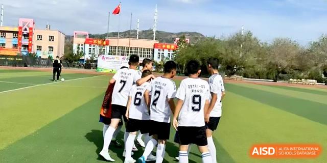 Teammates in white jerseys with black numbers celebrate together on the soccer field at Urumqi Bayi High School.