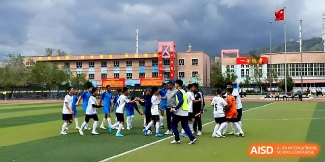 A large group of students in sports uniforms gathers for a team activity on the outdoor field at Urumqi Bayi High School.