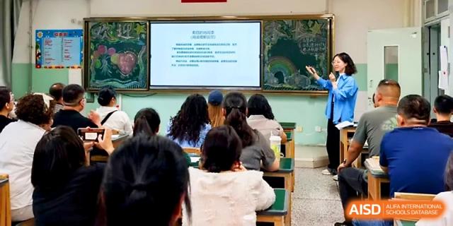 A teacher presents a digital slide to a group of parents or staff during an indoor meeting at Urumqi Bayi High School.