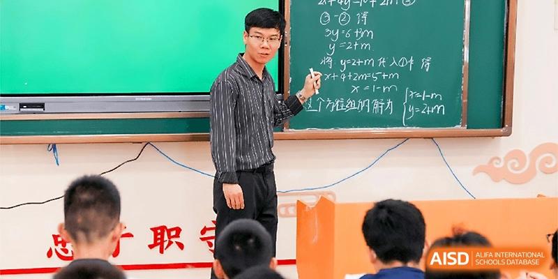 A male teacher in a striped shirt writes mathematical equations on a chalkboard for his students at Wuhan Guanggu Future School.