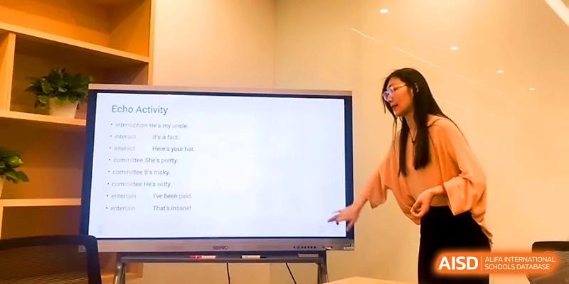 A teacher points to a digital smartboard while explaining a lesson to her class in a bright room at Wuhan Guanggu Future School.