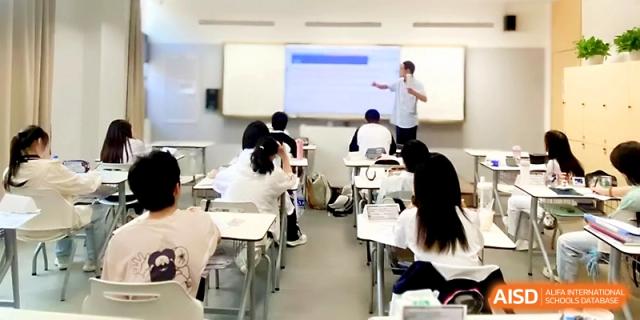 A teacher stands at the front of a modern classroom using a digital projector to explain a lesson to students at Wuhan Guanggu Future School.