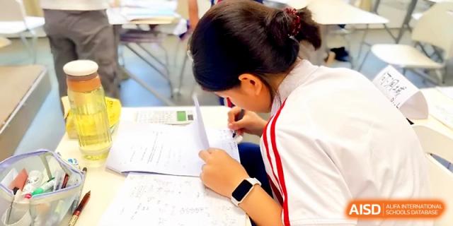 A student in a white and red uniform focuses intently on writing in a notebook during a quiet study session at Wuhan Guanggu Future School.