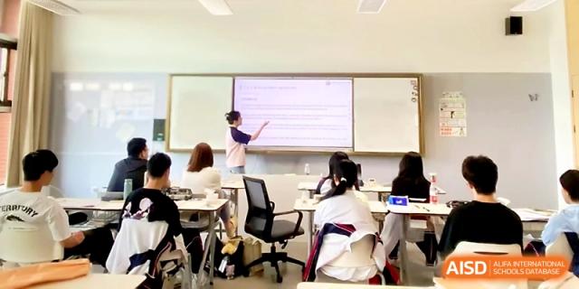 A student stands at the front of the class, pointing to a presentation on a large screen during a peer-led lesson at Wuhan Guanggu Future School.