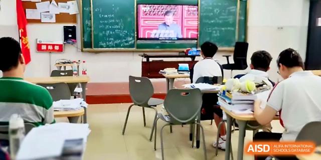 A student sits at a desk in a classroom, watching an educational video displayed on a screen at the front at Wuhan Guanggu Future School.
