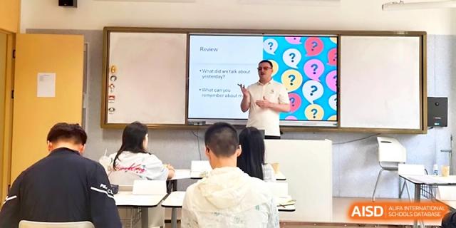An instructor gives an engaging presentation using a colorful digital slide to a class of attentive students at Wuhan Guanggu Future School.